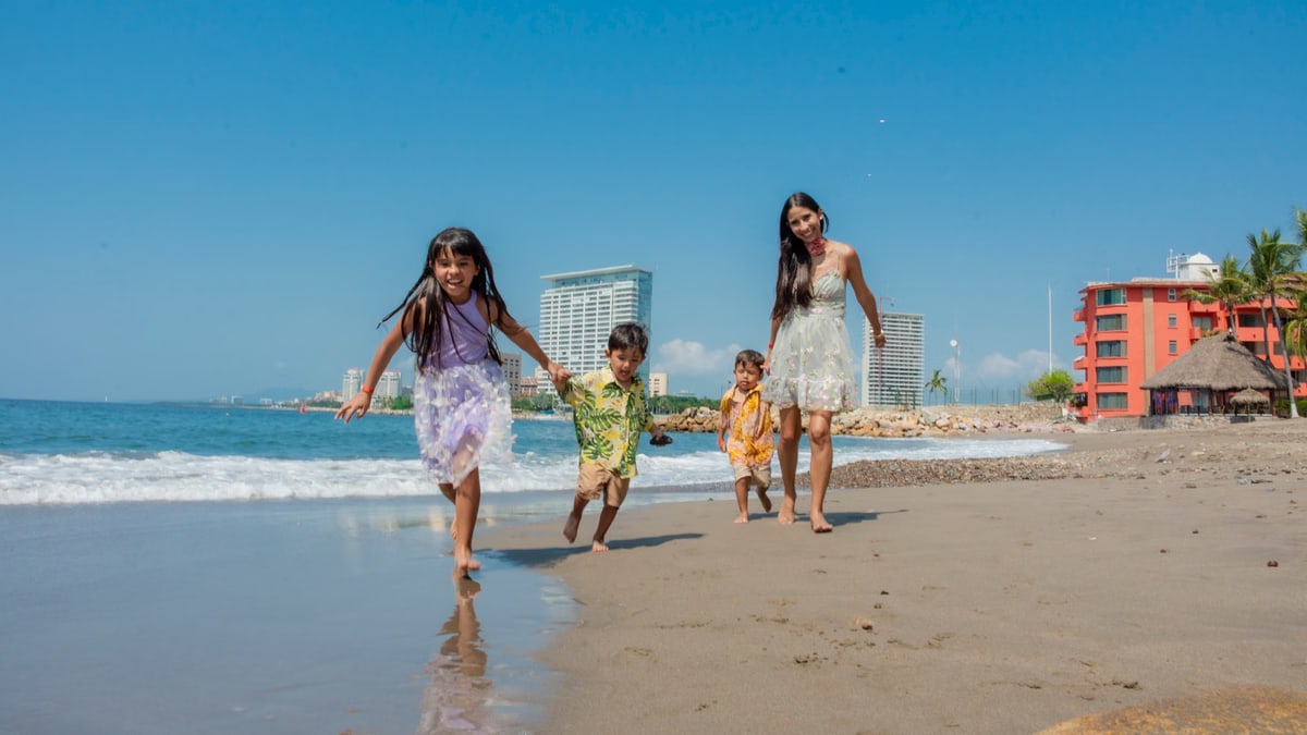 A joyful family playing on a sunny beach with waves and skyscrapers in the background.